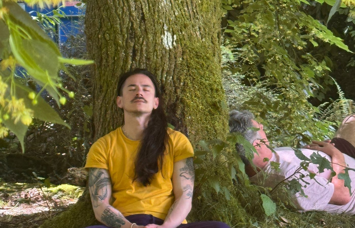 Participante en méditation adossée à un arbre pendant un stage en nature